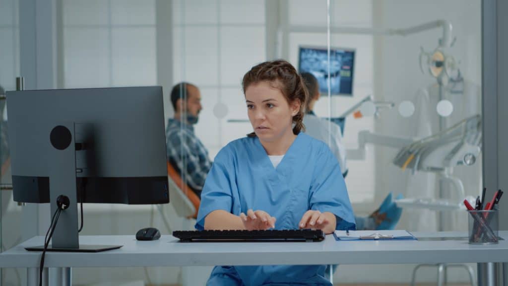 Dental assistant using computer and x ray scans at desk