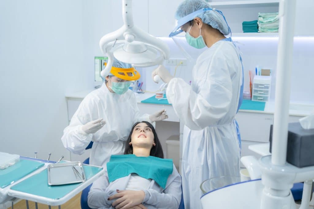 Doctor and assistant examining young woman patient's teeth or dental checkup at dental clinic.