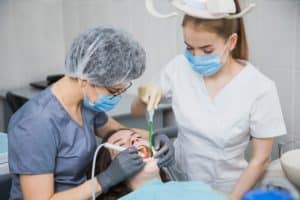 Female stomatologist curing dental cavity with assistant, patient on dentist chair